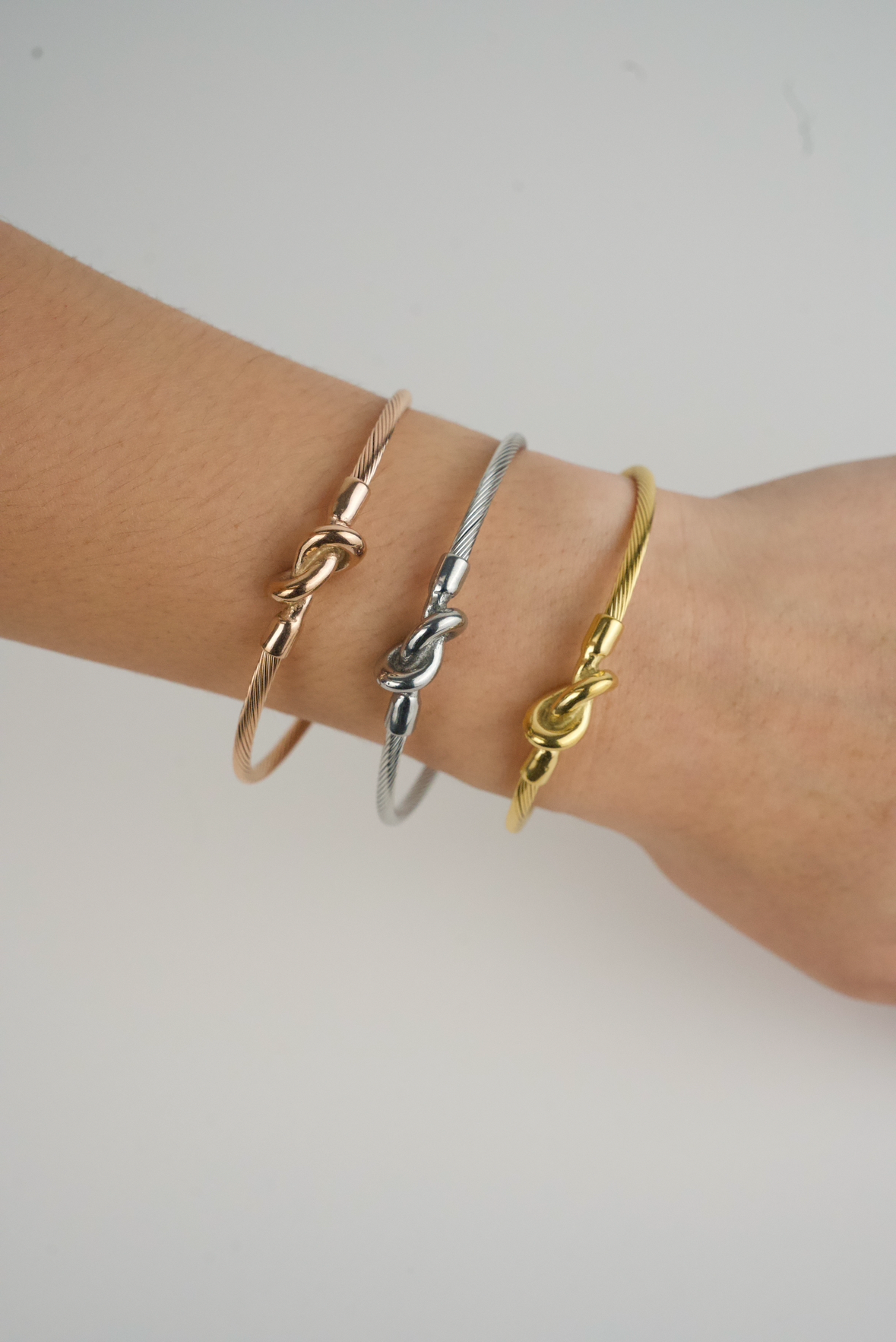 These are Charriol-style cable wire cuff bangles in silver, rose gold, and gold-tone stainless steel with a knot design.