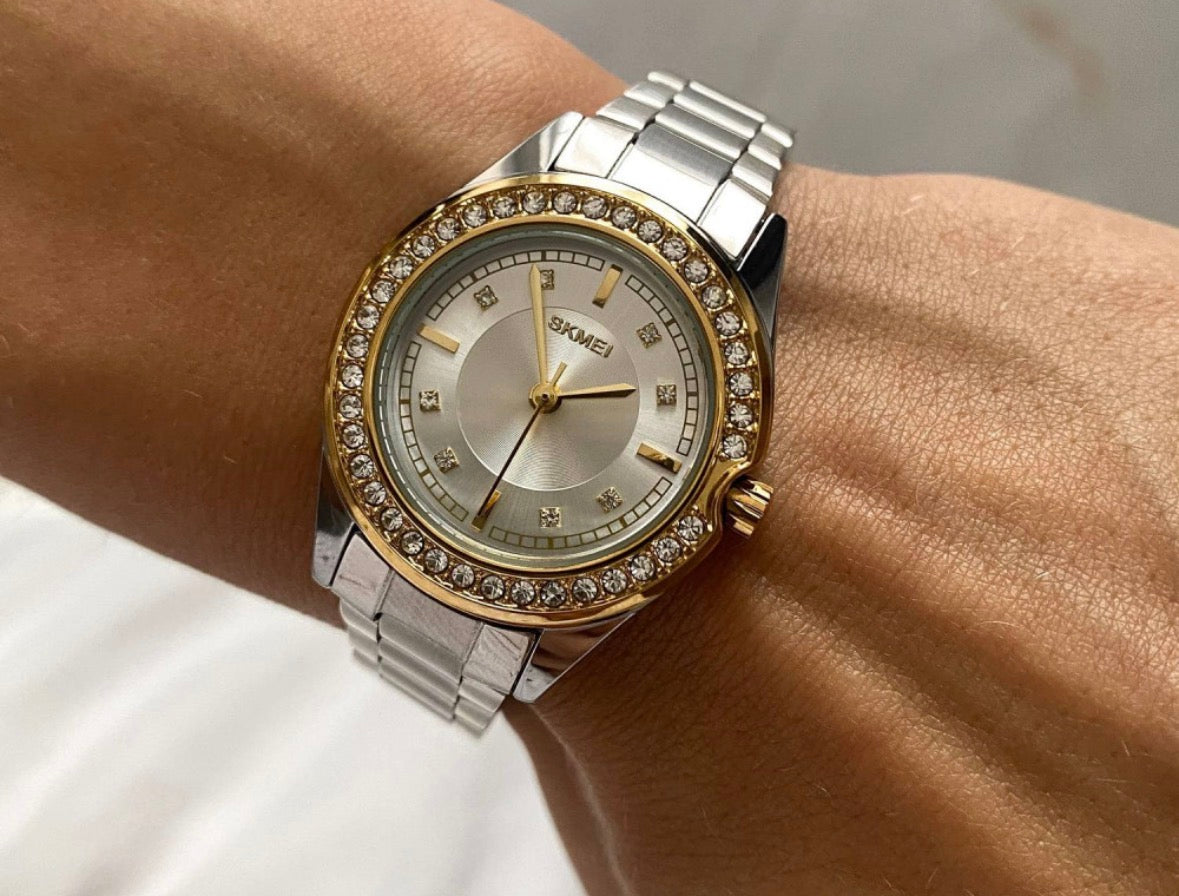This is a SKMEI 1534 women's quartz watch with a stainless steel band and a gold-tone, rhinestone-inlaid bezel