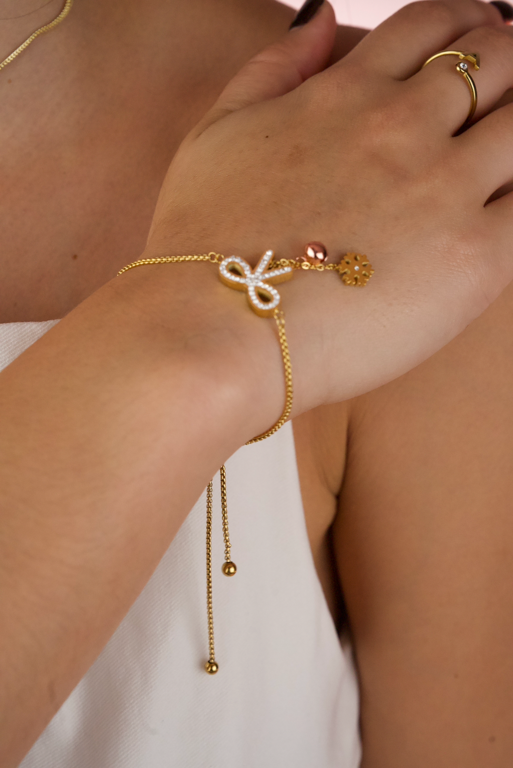 gold-finish adjustable chain bracelet featuring a pavé crystal bow motif and a small flower charm